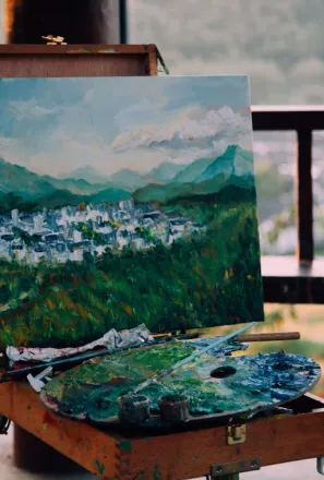 Creative artwork representing mounts and houses under sky near paint palette in wooden arbor