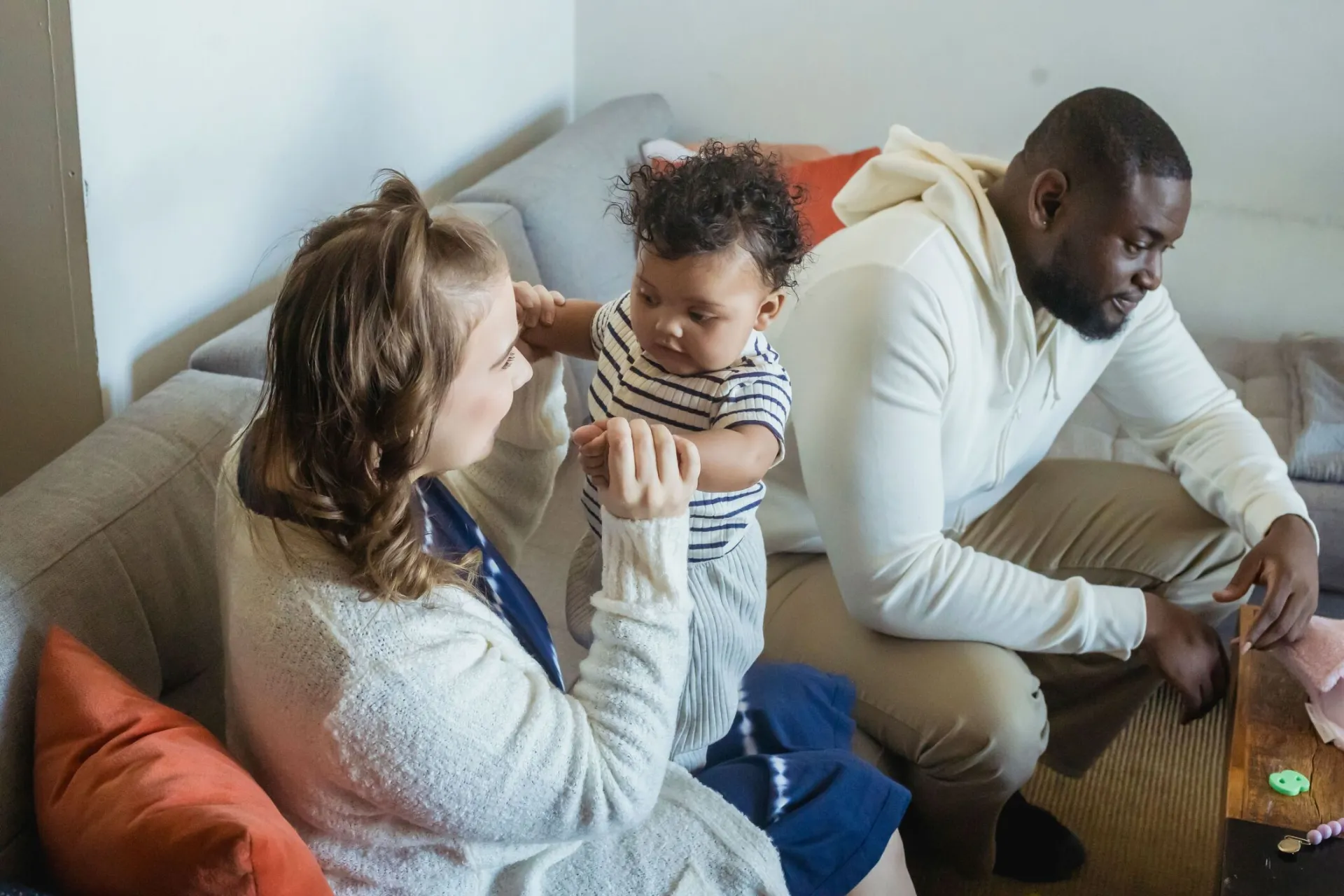 High angle of content mother with cute toddler child interacting on couch near black father in house