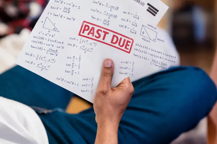 A man holding a past due billing statement while lounging indoors, expressing financial stress.