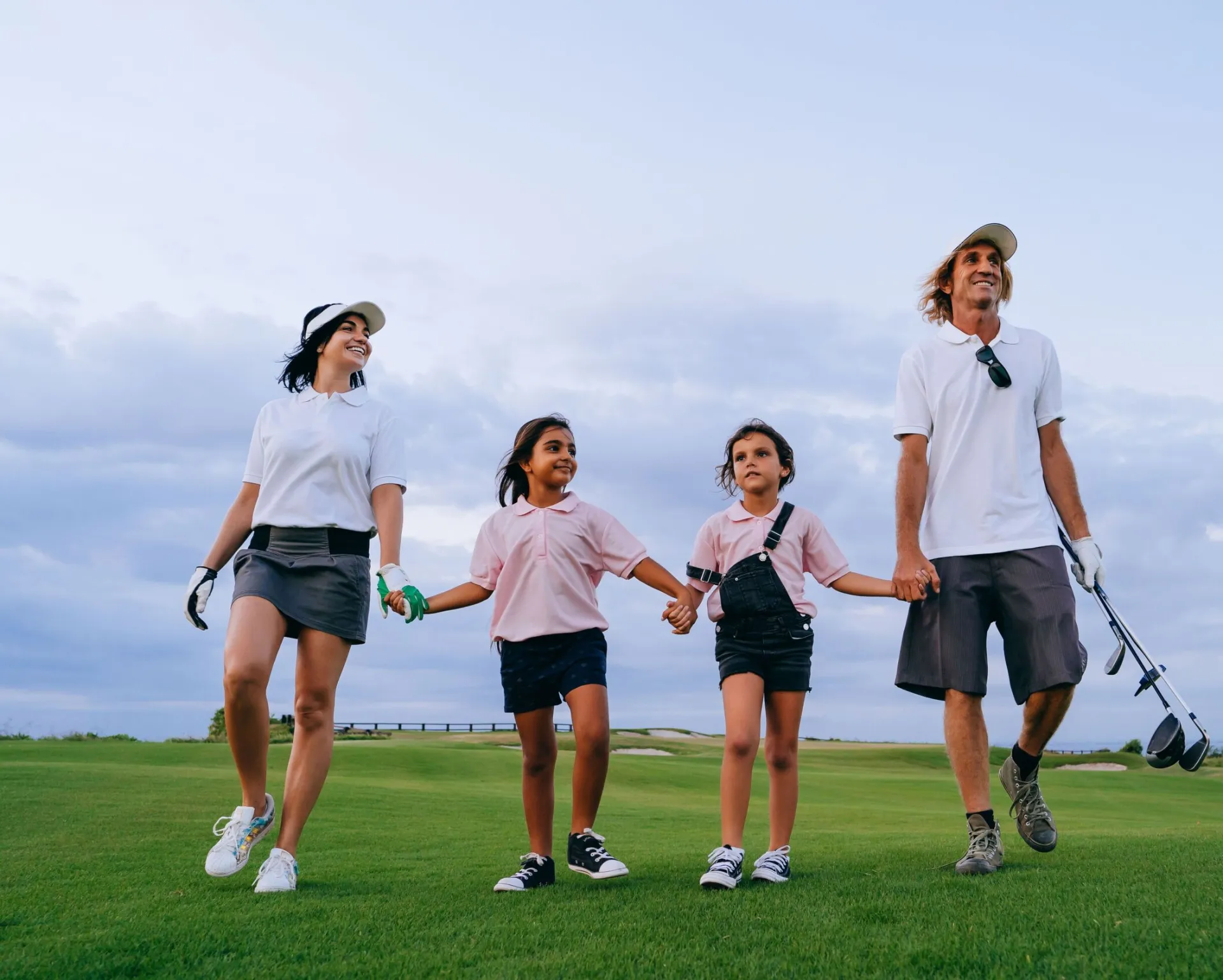 Happy family walking on a golf course together, enjoying leisure time outdoors with golf clubs.