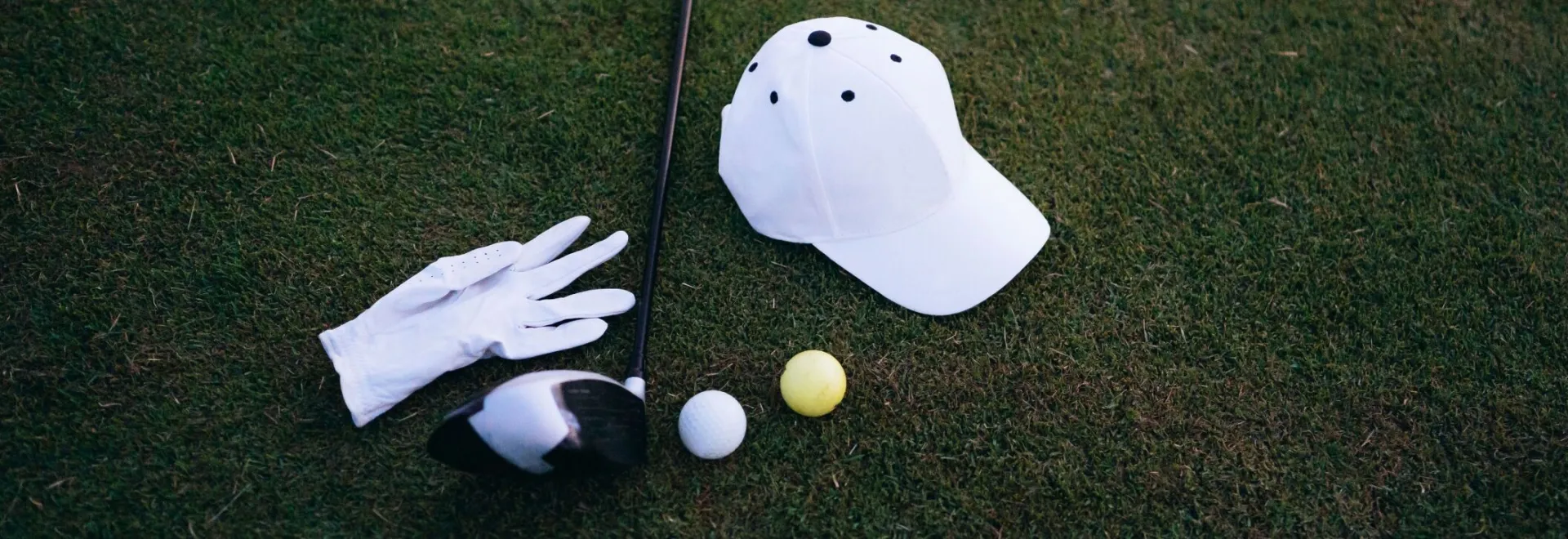 Close-up of golf club, balls, glove, and cap placed on green grass, perfect for a golf day.