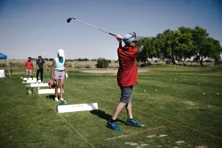 A group of youth practicing golf swings on a sunny day at the driving range.