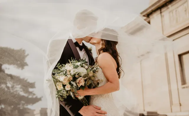 Bride and groom share a tender kiss under a veil, showcasing love and romance on their special day.