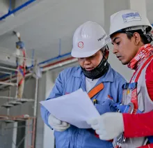 Two engineers in safety helmets reviewing construction plans at a worksite.