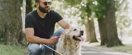 Blind man with guide dog in a lush park, highlighting companionship and support.